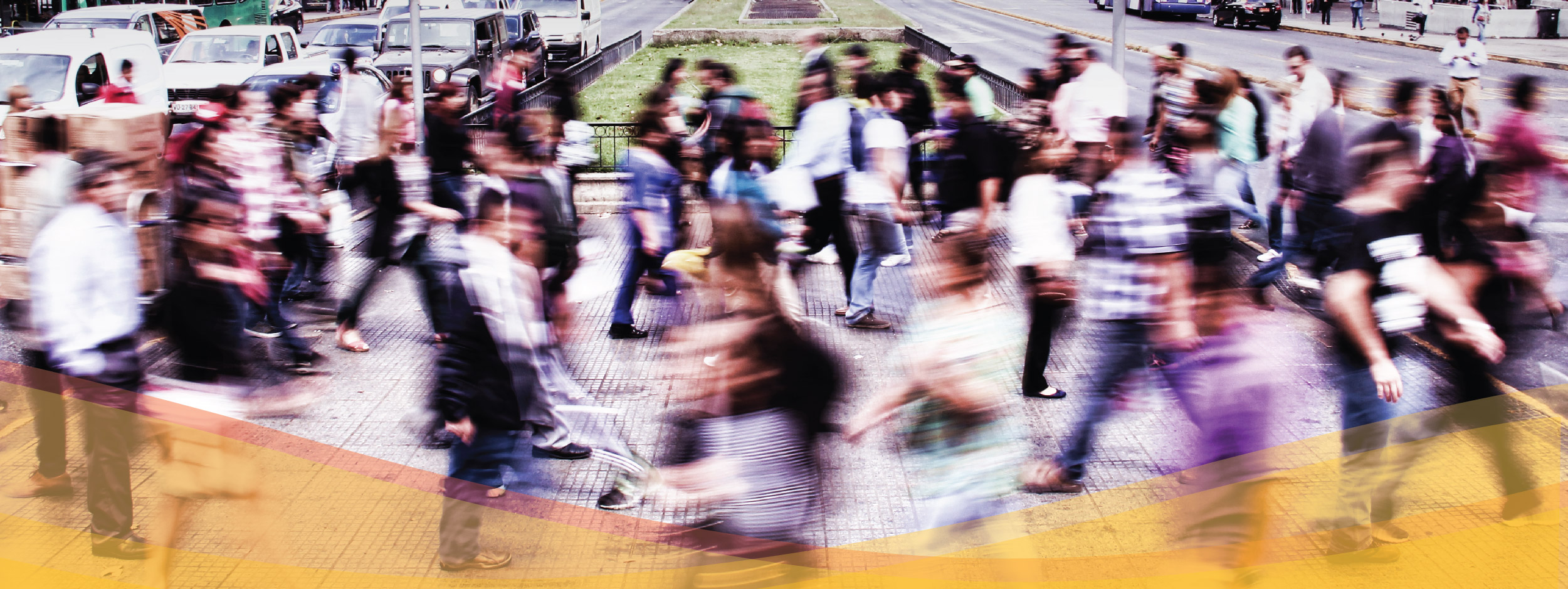 Dozens of people appear blurred as they move through a crosswalk in a busy city intersection. 